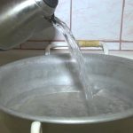 Versare acqua calda dal bollitore nella vasca di alluminio